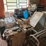 LOTE 008 - Sucata de mesas em madeira, classes e cadeiras escolares, caixas de som, aquecedor a óleo, fogão a gás, máquina de lavar, bebedouro, cama hospitalar, mesas ginecológicas, cadeiras de roda, cadeiras de escritório, máquina para confecção de fraldas e arquivo de aço